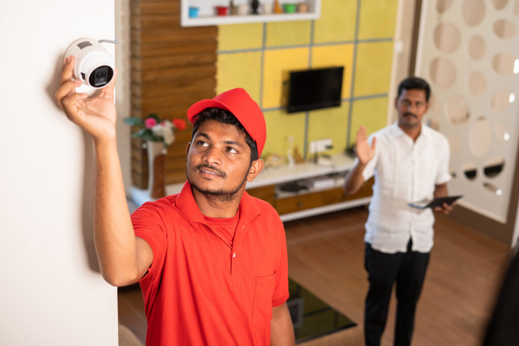 Technician fixing angle or view of cctv camera by while customer checking in digital tablet at home - concept of professional occupation, employment and surveillance